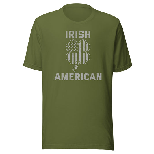 St. Pattys Day tee featuring the words Irish American in bold font with a clover leaf. The clover has an American Flag silhouette within it. Shirt color is olive green.